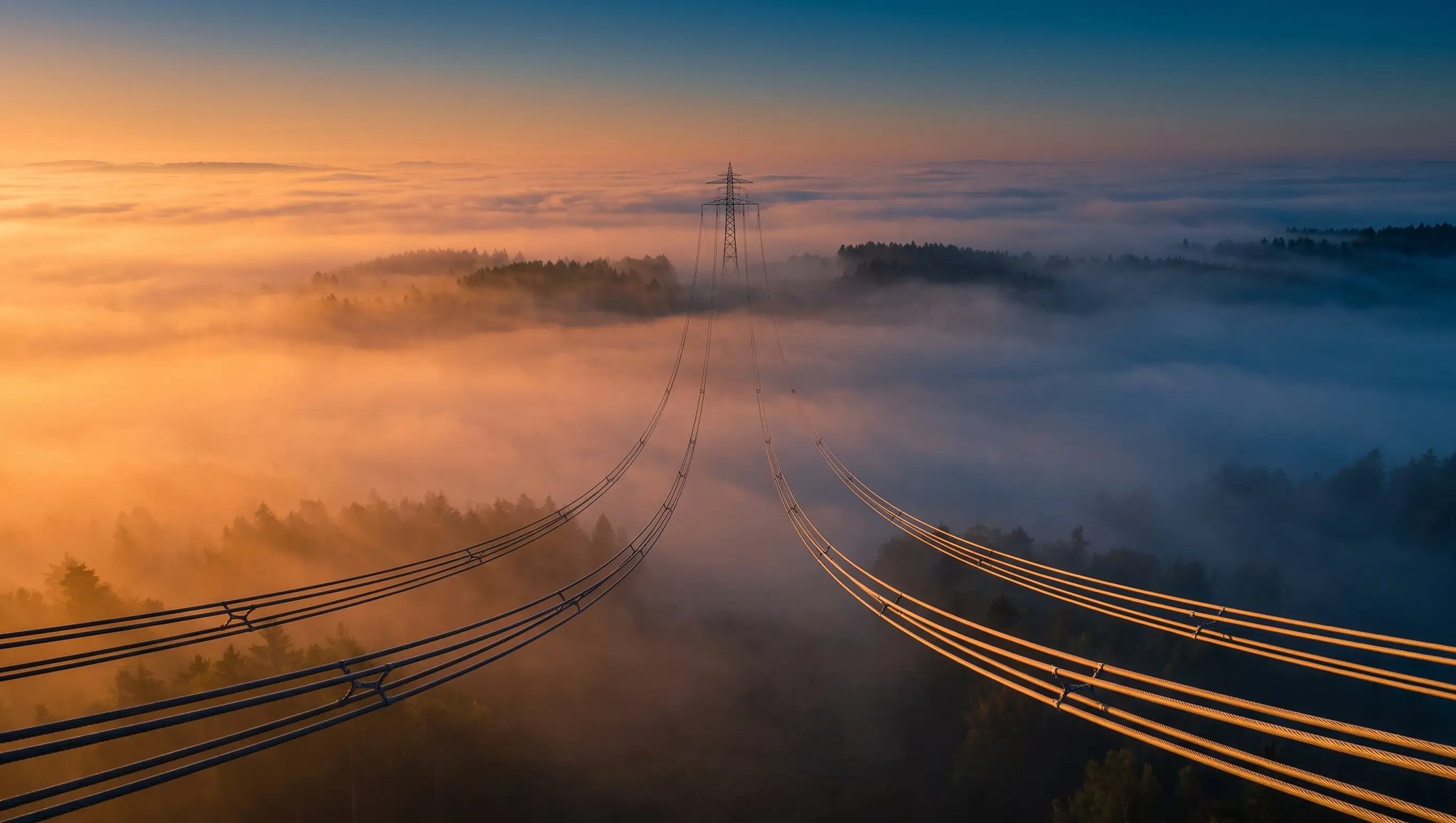 Blick von der Mastspitze entlang der Freileitung über dem Nebel – EnergyEng plant, steuert und sichert Freileitungs-, Trackway®- und Kabeltiefbauprojekte